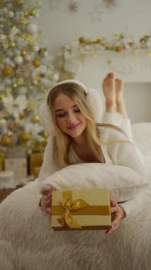 Sarışın bir kızın yeni yıl için hediye kutusu tutarken kameraya baktığı ön manzara. Güzel, neşeli kız gülümsüyor, eğleniyor. Mutluluk ve neşe kavramı.