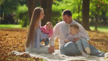 İki küçük çocukla yaz parkında piknik yapan genç bir ailenin yavaş çekim görüntüleri. Baba anneyi okşar ve çocuklarla oynar.
