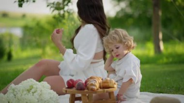 Yazın ailesiyle pikniğe giden sevimli sarışın bir çocuğun fotoğrafını çek. Beyaz çocuk battaniyenin üzerinde otururken tatlı yiyor. Mutlu bir çocukluk. Aile hafta sonu.