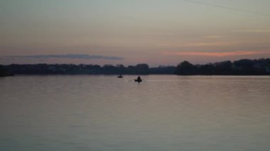 Gün batımında nehir boyunca yol alan bir tekne sahil boyunca martılarla çevrili.