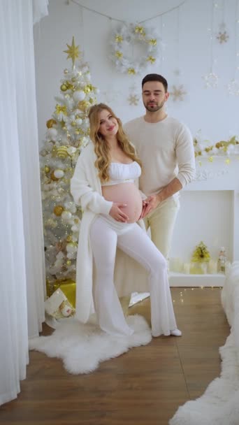 圣诞树上的幸福家庭丈夫拥抱他怀孕的妻子在美丽的装饰圣诞树附近 — 图库视频影像