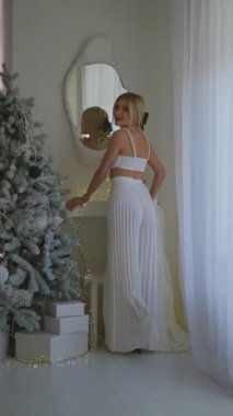 Beyaz elbiseli çekici bir kadının fantezi portresi. Güzel yüzlü, parlak makyajlı bir kız aynaya bakar. Model poz veriyor.