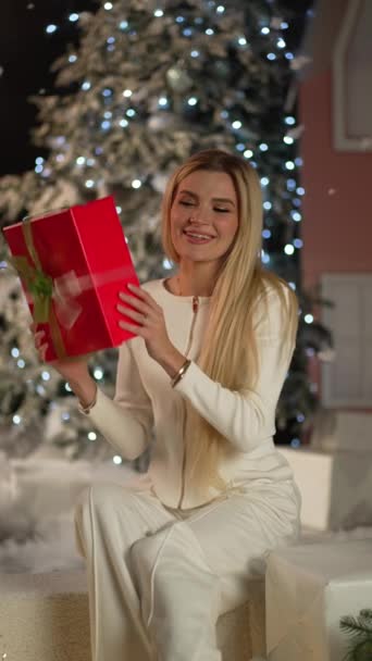 年轻女人摇着礼品盒 惊讶地看着装饰着圣诞花环的房间里的摄像机 — 图库视频影像