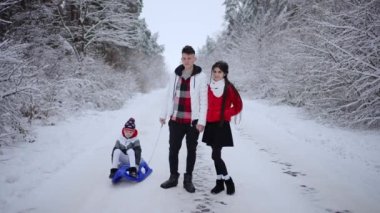Arkadaş canlısı aile tatilde kış ormanlarında yürüyor. Baba, anne ve oğul, karlı bir günde Noel tatili için dışarıda dinleniyorlar. Sıcak giysili insanlar. Yavaş çekim.