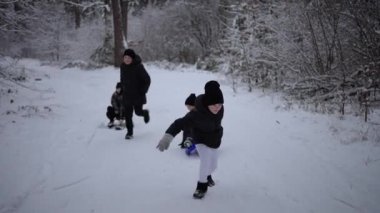 Çocuklar karlı bir tepede koşuyorlar ve kızak çekiyorlar.