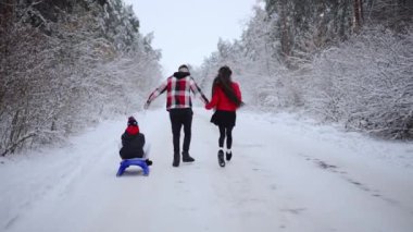 Baba ve anne oğullarını kış tatilinde kızakla gezdiriyorlar. Ebeveynler ve çocuklar, kış eğlencesi.