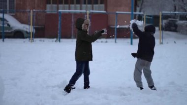 Sıcak giysili ve eldivenli çocuklar birbirlerine kartopu atıyorlar, bir kış günü bahçede birlikte oynuyorlar.