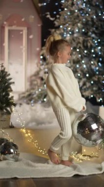 Sevimli küçük bir kız gülümsüyor, elinde parlak bir topla Noel ağacının yanında daireler çiziyor. Hediyesi olan mutlu bir kız çocuğu. Kış tatili.