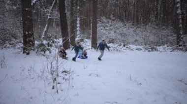 Bir aile kış ormanında yürür. Ormanda kızak kayarken