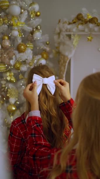 2人の若い女の子が鏡の前に立って 髪に弓を固定し 新年を祝う準備をしている リアビュー — ストック動画