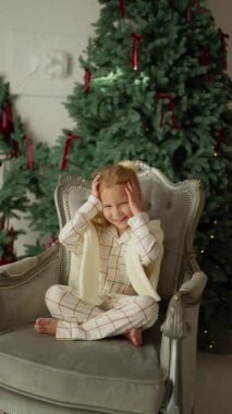 Sandalyedeki neşeli küçük kız Noel Baba 'dan yeni yıl hediyesi bekliyor.