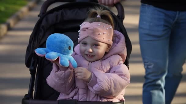 Criança Feliz Sorrindo Segurando Brinquedo Enquanto Monta Uma Carruagem Bebê — Vídeo de Stock