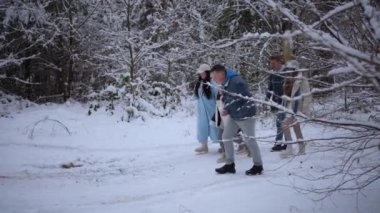 İnsanlar karlı ormanda el ele tutuşmuş çocuklarıyla eğleniyor.