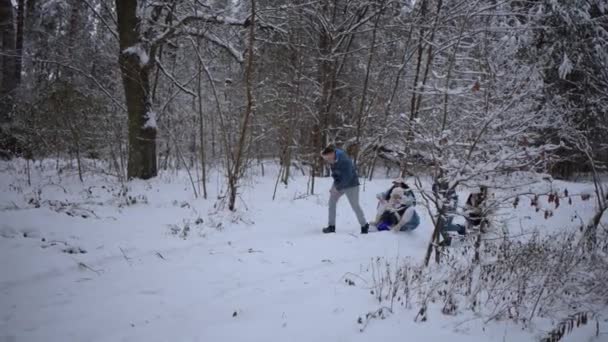 少女と陽気な女性とソリを引っ張る幸せな男性のスローモーション追跡ショット 家族は森で冬の日を楽しんでいる — ストック動画