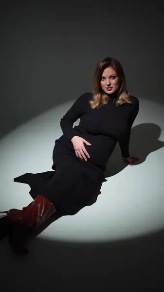 Siyah elbiseli çekici hamile kadın yerde yatarken fotoğrafçıya poz veriyor.