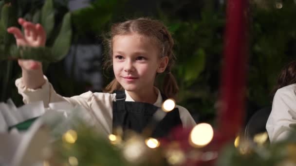 小さな笑顔の女の子がクリスマスの花輪を作っています 冬と新年のコンセプト — ストック動画