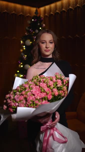 黑衣女子手持一大束粉红玫瑰 背景为圣诞树 — 图库视频影像