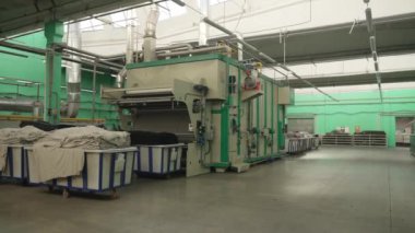 Çamaşır odasının geniş bir manzarası var. İçinde büyük makineler ve keten arabaları var..