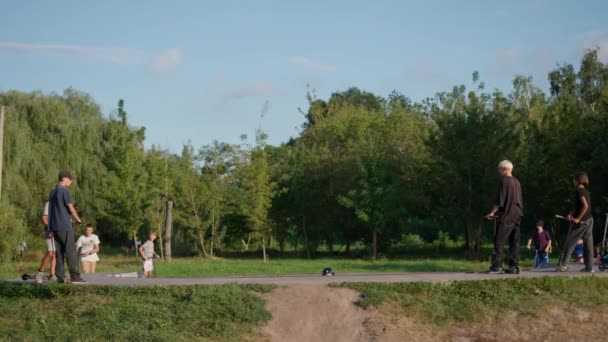 무성한 녹지로 둘러싸인 공원에서 스케이트 보드와 스쿠터를 젊은이 — 비디오