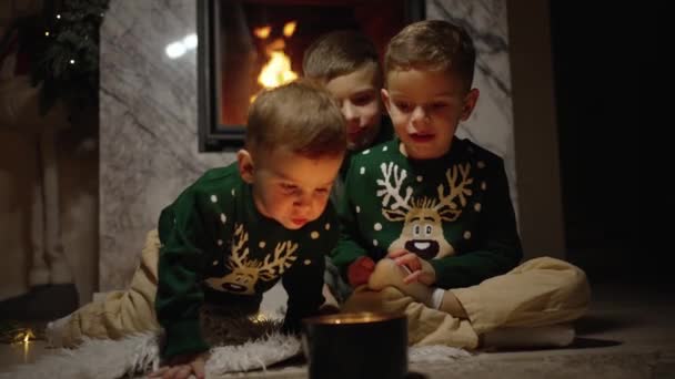 Μικρά Αδέλφια Γιορτινά Πουλόβερ Ταράνδων Κάθονται Δίπλα Στο Τζάκι — Αρχείο Βίντεο