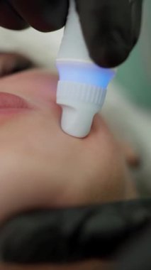 Eldivenli güzellik uzmanı kozmetoloji kliniğinde genç bir kadının cildini temizleyip cilalıyor. Modern insanlar için profesyonel nemlendirici ve gençleştirici donanım prosedürleri.