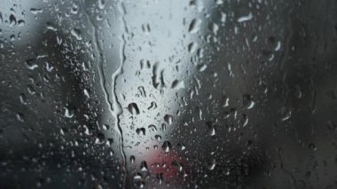 Yağmur damlaları alacakaranlıkta şehrin bulanık arkaplanıyla pencereye hafifçe düşer