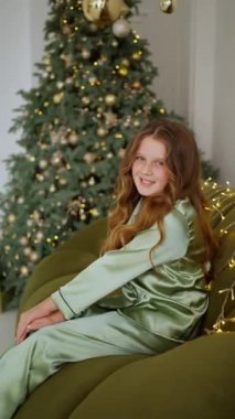 Arka planda Noel süslemeleri olan pijamalarıyla oturan sevimli küçük kız.