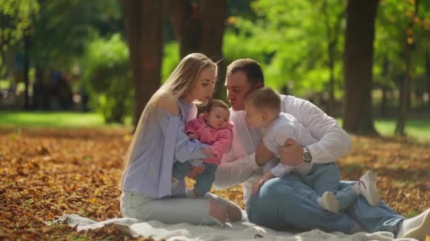 親から子供への優しいキスは 秋の日の鮮明さに包まれた公園の毛布に密接に座っているので この家族の愛の絆を象徴しています — ストック動画