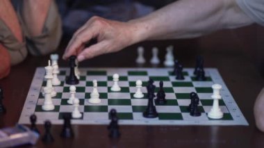 Yaşlı ellerin hamle yapmasıyla devam eden bir satranç tahtası oyununun yakın çekimi.