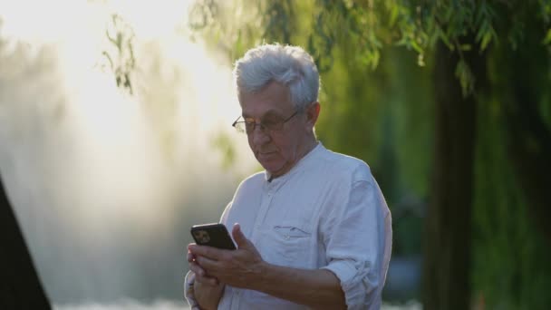Gözlüklü Yaşlı Adam Güneşli Parkta Cep Telefonuna Odaklandı — Stok video