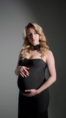 Siyah elbiseli hamile kadın fotoğraf çekiminde poz veriyor..