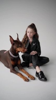 Şık giyimli, tatmin edici ifadeli mini model tasmalı köpeğin yanında oturuyor..