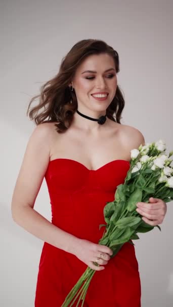 輝く笑顔は彼女のストラップレスの赤いドレスを補完し 彼女は新鮮な白いブーケを握り シーンに自然なエレガンスのタッチを追加します — ストック動画