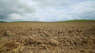 Bulutlu bir gökyüzüne karşı hasır kalıntılarıyla tarlaya sürülmüş kahverengi toprak..