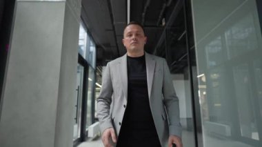 Akıllı telefonunu dikkatle kontrol ediyor, bir işadamı koridorda geziniyor, kurumsal bir ortamda modern bir çoklu görev..