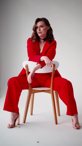 内観的な視線で 女性は木製の椅子に赤いスーツで彼女のポイズシートを展示し 彼女の外観はミニマリストのヒールで完成しました — ストック動画