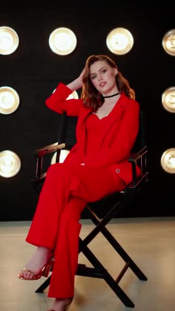 在温暖的圆形灯光下 当她坐在导演的椅子上 女人的笑容与她的红色西装和窒息的衣服相得益彰 — 图库视频影像
