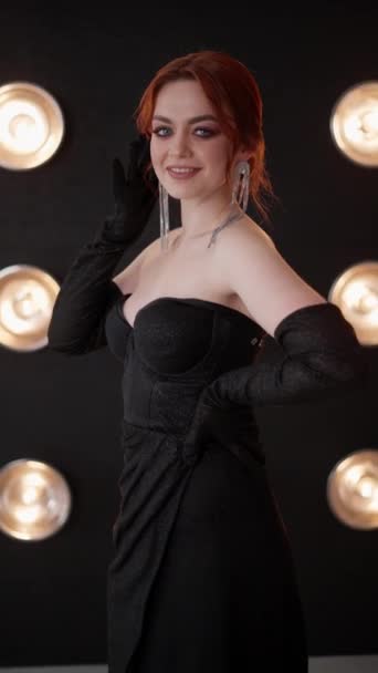 一个女人穿着漂亮的黑色长袍 配以闪闪发光的长耳环和精致的手套 站在柔和明亮的灯光下 — 图库视频影像