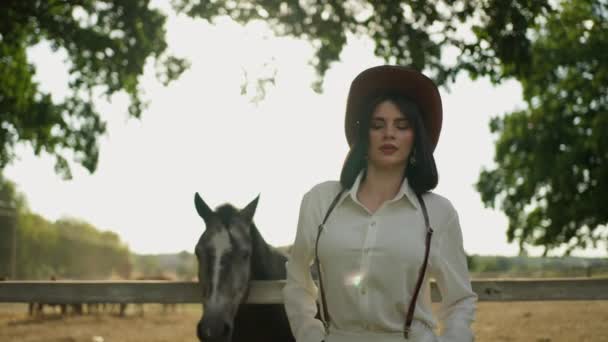 スタイリッシュな帽子の女性は日没時に馬と一瞬を共有します — ストック動画