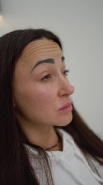 Bir müşteri, klinik bir ortamda profesyonel değerlendirme için alnındaki çizgilerin altını çizerek cilt bakımı konusundaki endişelerini dile getirir..