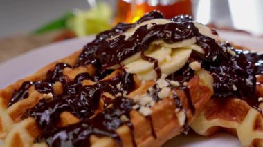 Lezzetli bir Belçika waffle 'ı, tatlı bir ziyafet için mükemmel bir tabakta, çikolata ve ezilmiş fındık serpiştirilmiş cömert bir tepsi alır..