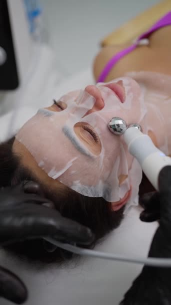 技術的な治療装置とシートマスクを慎重に統合するこの手順は 伝統的で現代的なフェイシャルケア方法のシナジーを例示します — ストック動画