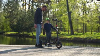 Babasıyla dışarıda scooter sürmeyi öğrenen küçük bir çocuk. Şirin küçük çocuk ve baba dışarıda eğleniyorlar..