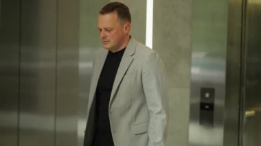 Takım elbiseli bir adam asansör koridorunda yürür, kurumsal karmaşanın ortasında yalnızlığı somutlaştırır..