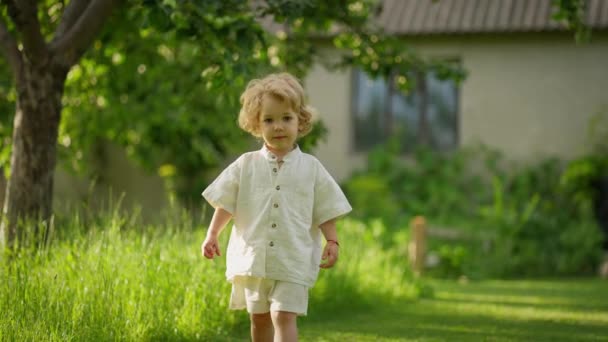 その明るい夏の日 ベージュの衣装の子供は庭で幸せに走っています — ストック動画