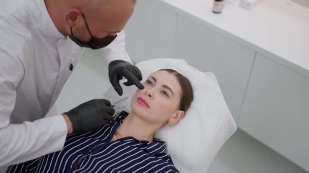 Kosmetolog Rękawiczkach Ostrożnie Wstrzykuje Skórę Kobiecej Twarzy Leżącej Kanapie — Wideo stockowe