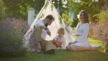 Ebeveynler ve küçük oğulları, akşam ışığında lavanta tarlalarıyla çevrili çadırın yanında karpuzun tadını çıkarırlar..