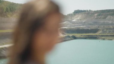 Kadının gözlerinde neşeli bir parıltı, saçları rüzgarla dalgalanmış, gölün kıyısındaki bulanık sükunetin arka planına karşı..