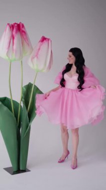 Yetişkin, güzel, esmer bir prensesin portresi pembe bir gece elbisesiyle çiçeklerin güzelliğinin tadını çıkarıyor..
