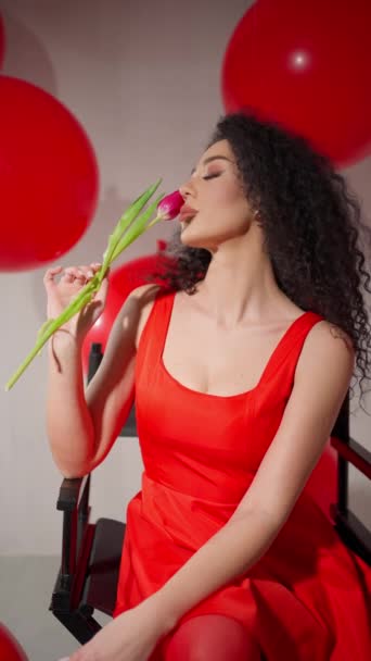 穿着红色衣服和高跟鞋的优雅女人坐着 凝视着一朵郁金香 周围围着红色的气球 — 图库视频影像